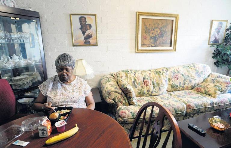 Barbara Hatcher, who lives alone in McAfee Towers, enjoys a lunch at her apartment brought by a Meals on Wheels staffer. Hatcher says the human contact is at least as nutritious as the crab salad, fruit and chocolate milk meal.