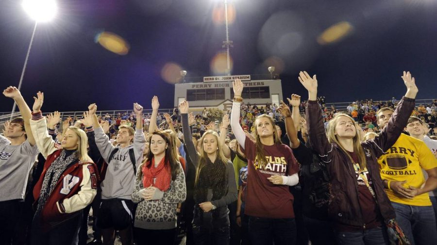 Students sway their arms as a praise band with Central Baptist Church in Warner Robins performs during a 2012 Fellowship of Christian Athletes Fields of Faith event at Perry High School’s Herb St. John stadium.