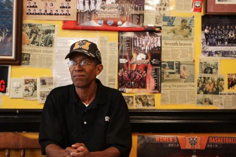 Carl Fambro sitting in front of one of his Mercer University memorabilia filled walls. His favorite part about owning a restaurant is the community involvement and connecting the people of Mercer Village with his chicken wings.