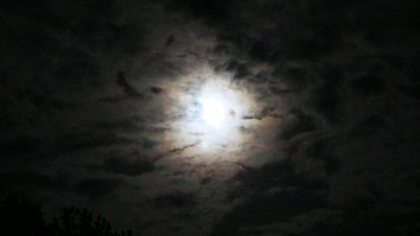 The moon is hidden behind a sheet of clouds, causing it to appear like a spotlight in the night sky. 