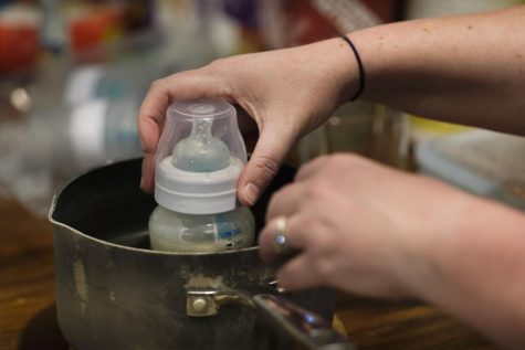 Maggie Reimer swirls a baby bottle in a pot of hot water.