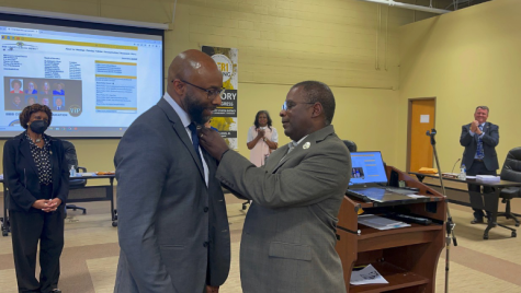 Superintendent Curtis Jones, left, secures a Victory in Progress pin to incoming Superintendent Dan Sims coat at the May 10 meeting solidifying Sims as the districts next leader.