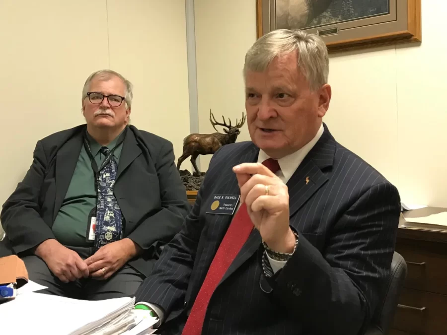 Dale Folwell talks to reporters about hospital prices in June 2022. Behind him sits interim State Health Plan director Sam Watts.
