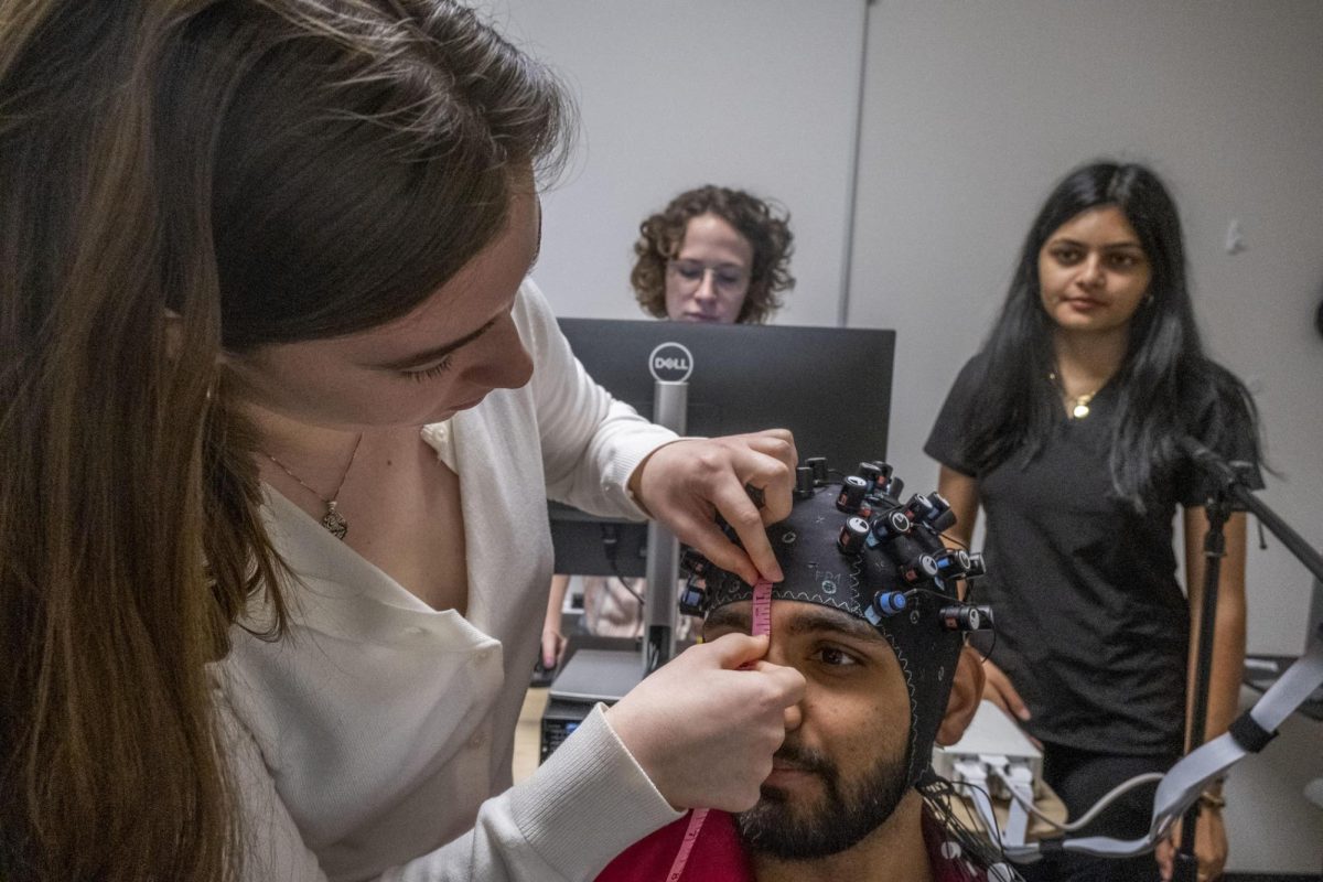 Classmates watch as Mercer University student Grace Gasaway fits a functional near-infrared spectroscopy cap onto student Parth Patels head. Unlike the stillness required for an MRI machine, researchers can map brain activity using fNIRS while participants are moving around, making it ideal to use on young kids.
