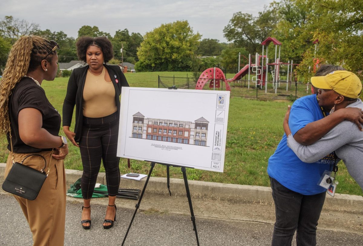 Pleasant Hill residents and an architectural rendering of an apartment block planned for the lot with the playground behind them after the announcement of Pleasant Hill Landing Sept. 19, 2024.