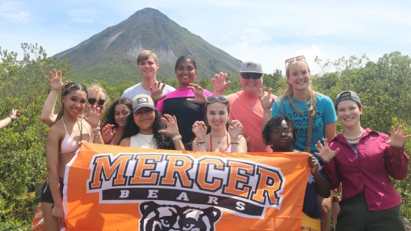 A 2025 Spring Break study abroad group posing with a Mercer flag at Arenal National Park & Volcano in Costa Rica.